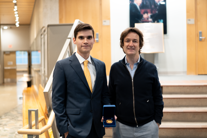 Jorge Holguín Cruz stands, holding his medal, next to his graduate supervisor Dr. Jörg Gsponer in the lobby of the Michael Smith Laboratories building.