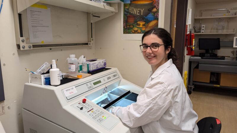 PhD candidate Sarah Ebert smiles to camera, sitting down at an instrument in the lab.